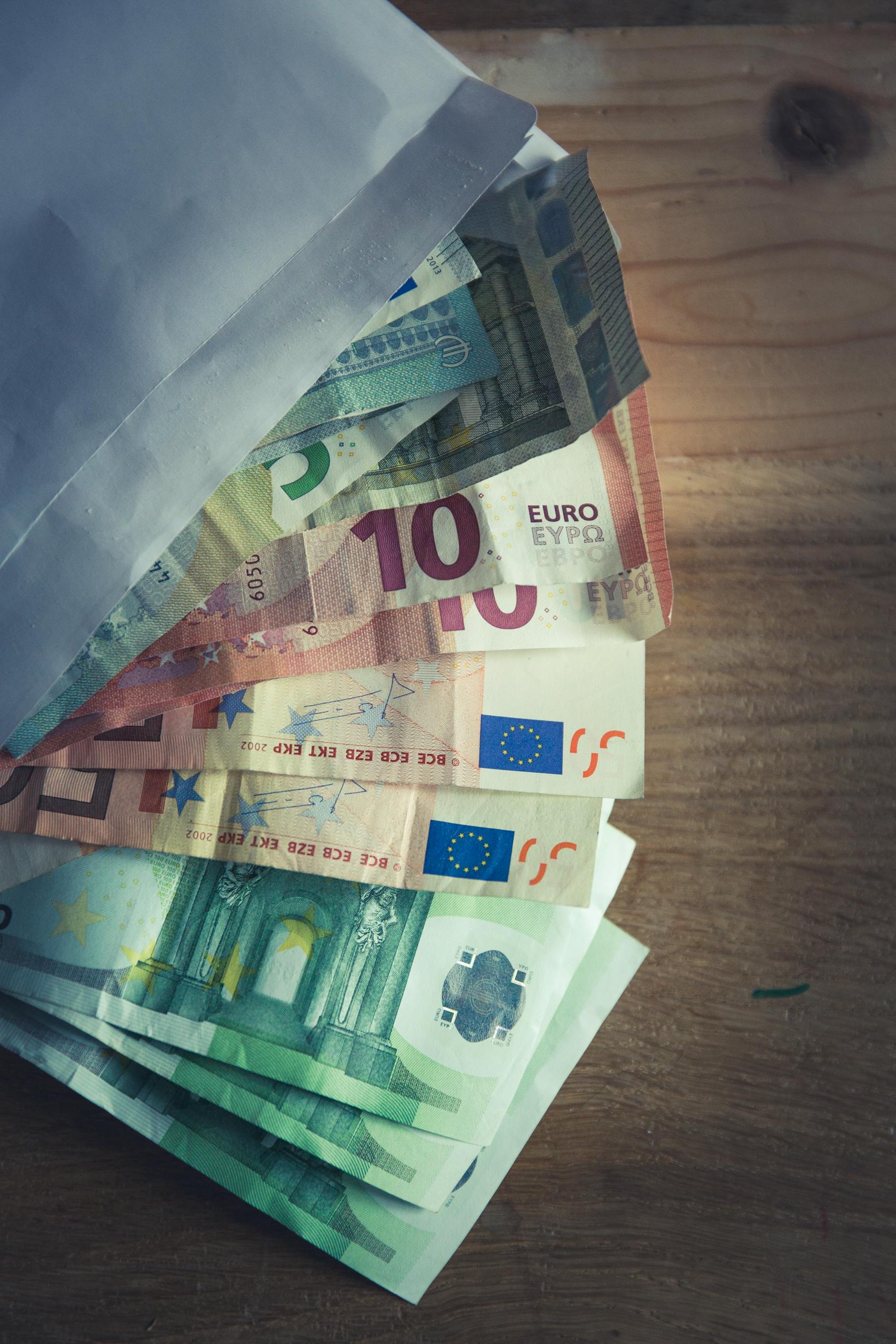 A collection of Euro banknotes emerging from an envelope on a wooden surface.
