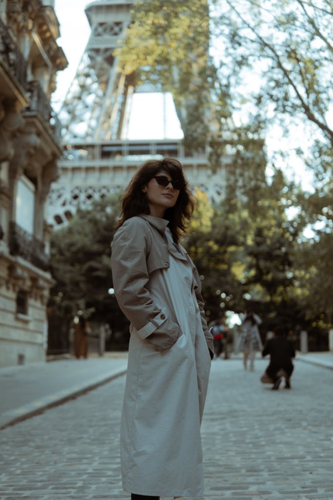 Stylish woman in a trench coat stands near the Eiffel Tower, capturing Parisian elegance.