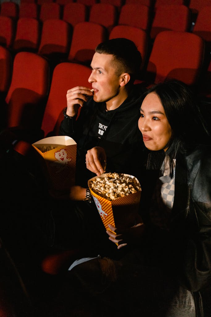 A couple seated in a cinema enjoying popcorn during a movie night.