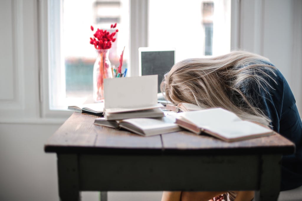 Aplicando-se ao post "Melhore seus estudos - 5 erros para evitar, uma mulher esta com o rosto encostado em uma mesa cometendo assim o primeiro erro - a procrastinação