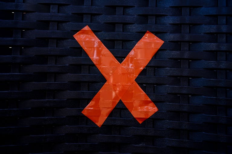 Close-up of a red tape cross on a black woven rattan surface, highlighting contrast and texture.