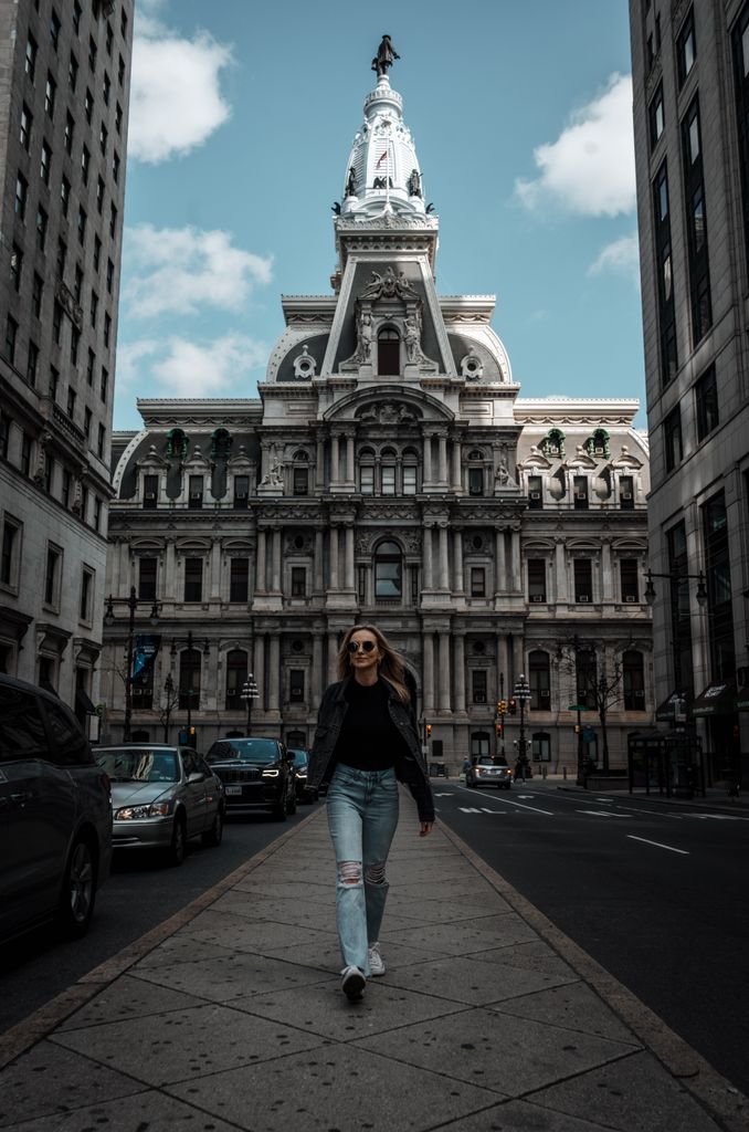 A stylish woman walks confidently in front of Philadelphia City Hall, showcasing urban fashion.